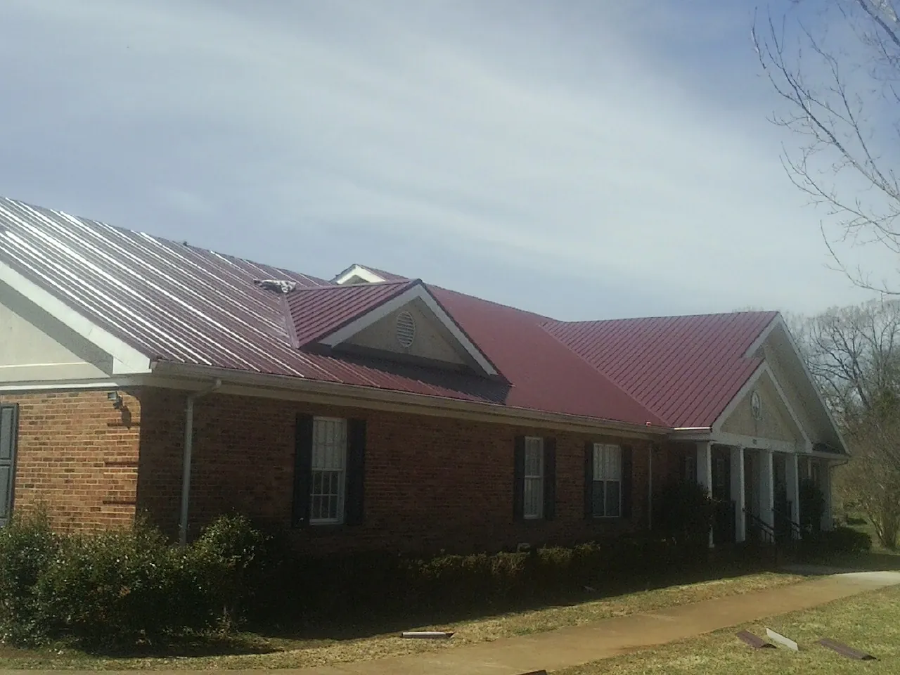 Red metal roof with gabled entries on a long brick building, from a Hail Damage Roof Repair job in Chocowinity