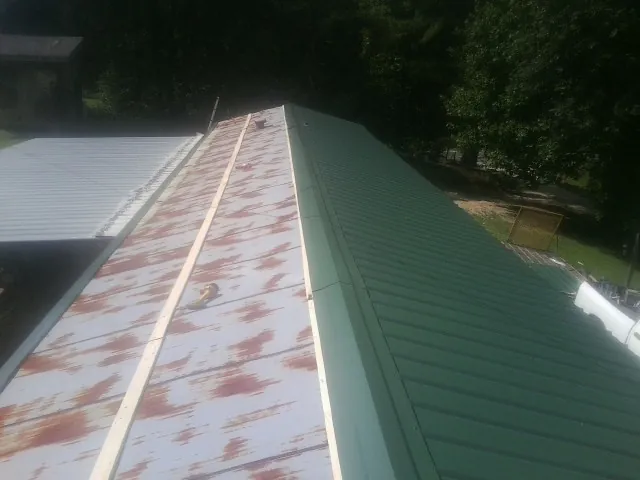 Old rusted panels beside newly installed green metal roofing — Wind Damage Roof Repair by Roofing Brothers in Chocowinity