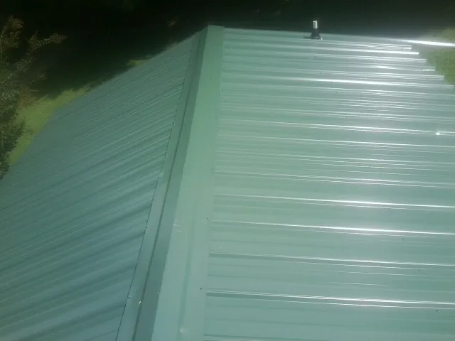 New green metal panels meeting at the ridge of a roof — Flat Roof Repair work by our crew in Chocowinity